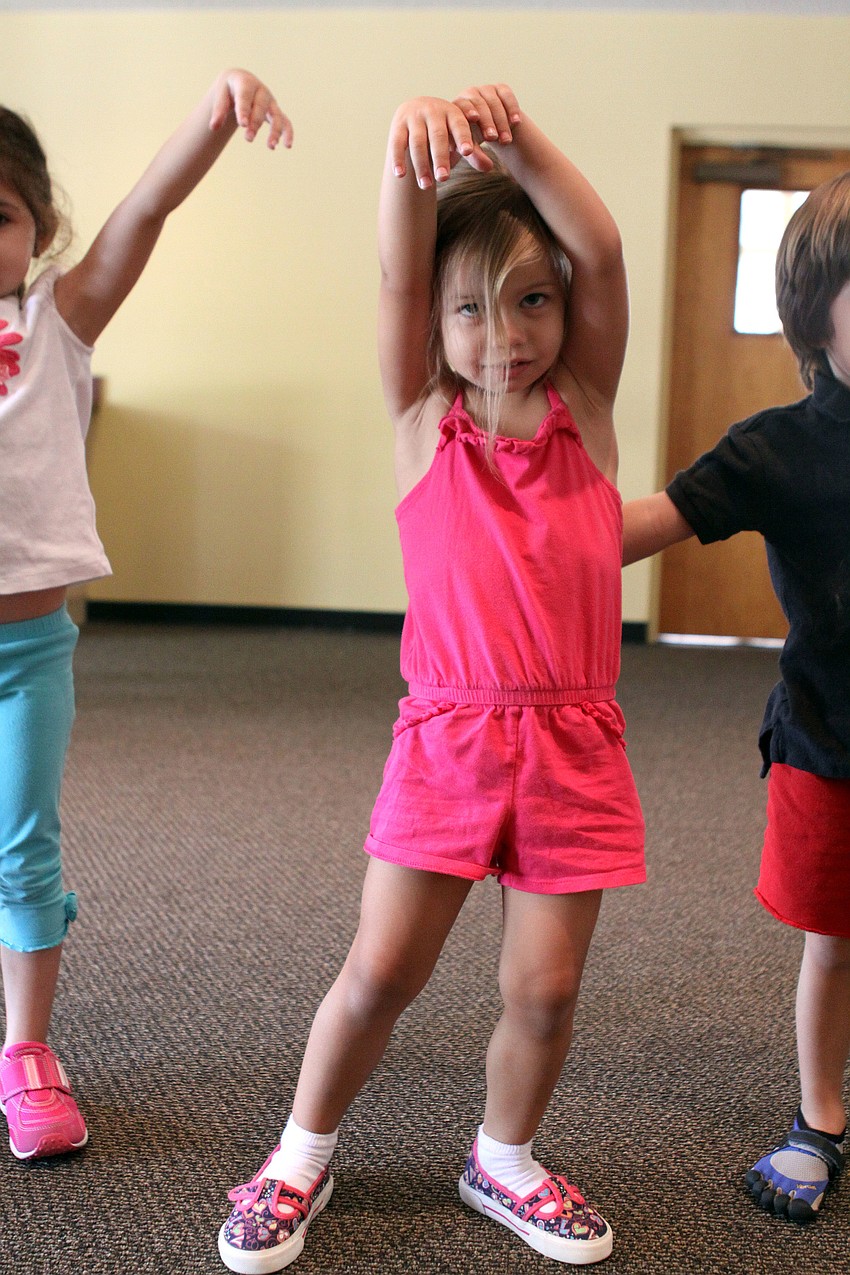 Chesney Beckman raises her hands up over her head and pretends to be a tree swaying in the breeze.