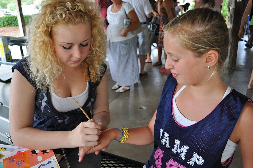 Marylyn Meyers paints a pink flower on the hand of Jolie Mallitz.