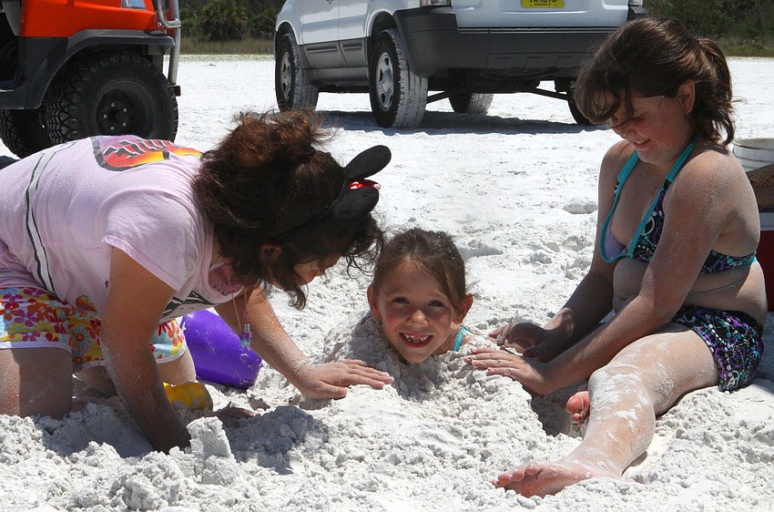 Annie Baez, 10, and Natalia McNabb, 10, bury their friend Jaymie Hager, 6, Saturday, May 5, during the 40th Sand Sculpting Contest.
