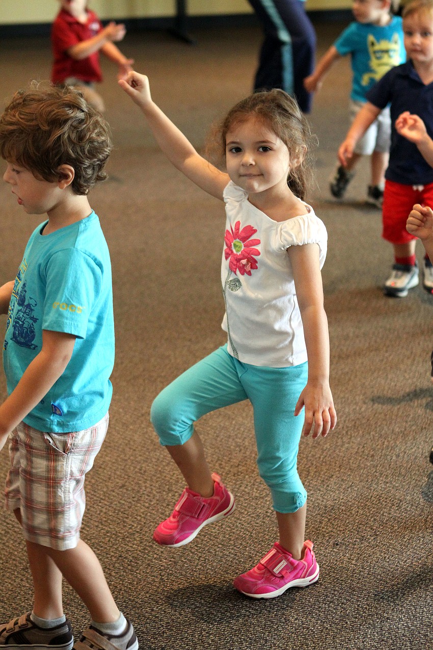 Helene Giraud raises her arm as if she were holding a flag while she marches around the room.