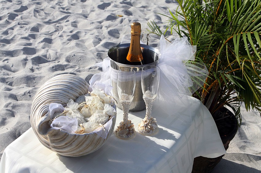 A side table at the wedding had a bowl shaped like a shell containing little packets of heart-shaped, bird-friendly rice, a bucket with ice and champagne and two, decorative champagne glasses for the special couple.