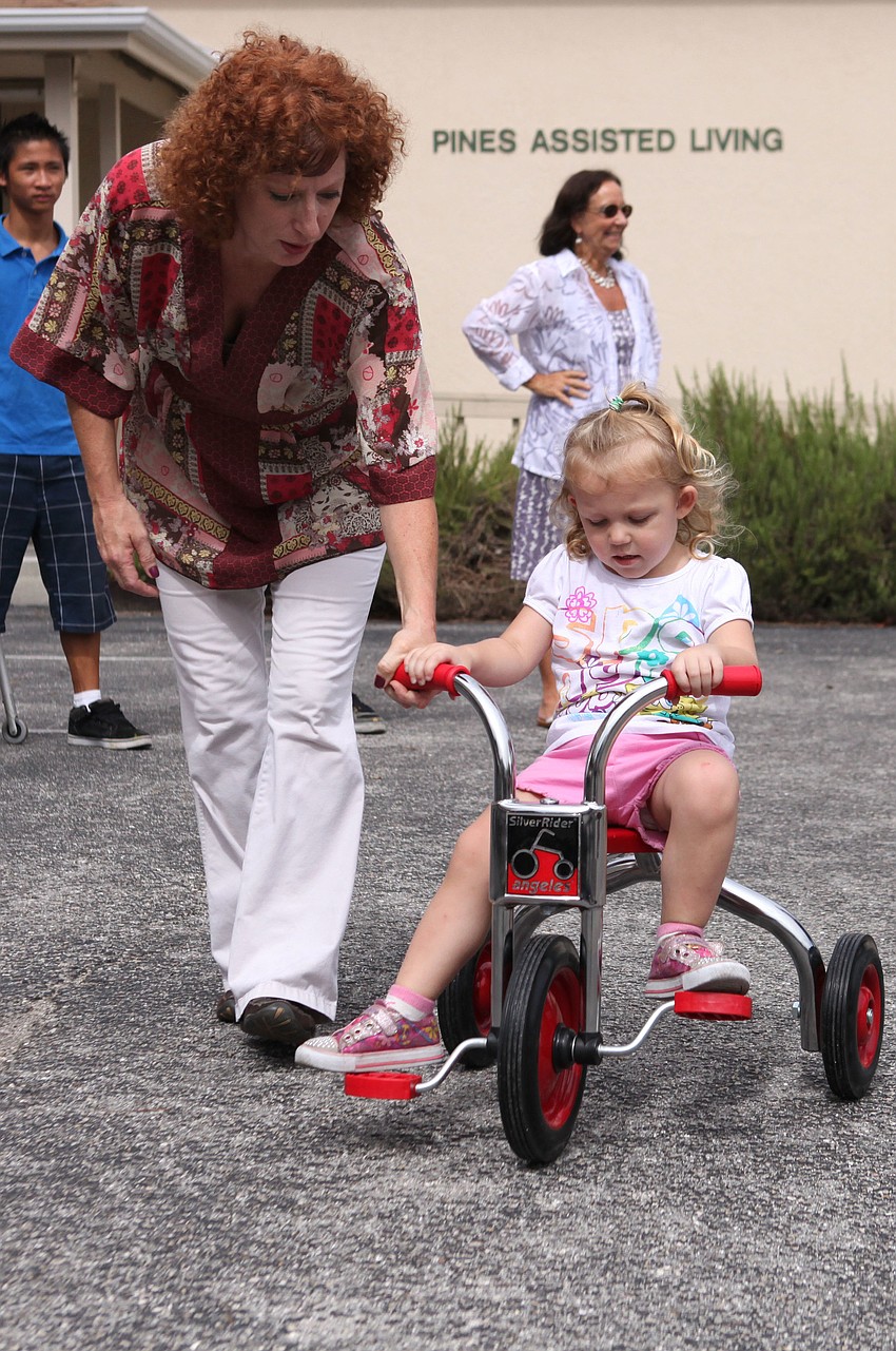 Ruth Martin helps Rylee Wyant, 2, ride one of the tricycles.