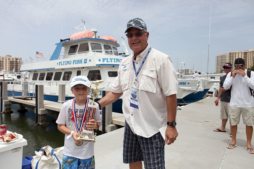 Tryston Passon poses with his trophy for â€œlargest fishâ€ with Alan Anderson, Wednesday, Aug. 8. Passon caught a red grouper while participating in the Kids Klub Fishing Tournament that happens in conjunction with the Sarasota Slam.