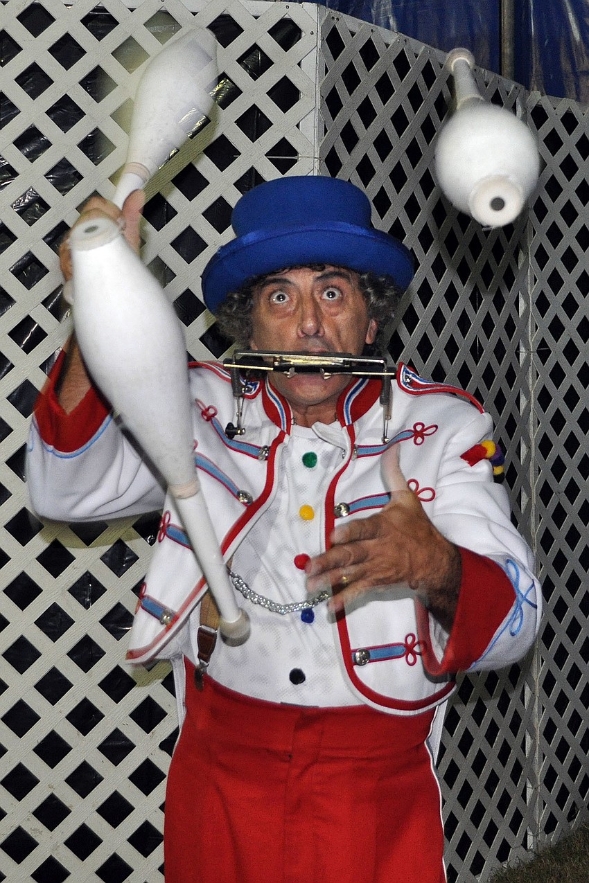 Marcelo Spaghetti the Clown plays the harmonica while juggling bowling pins.