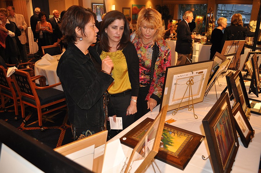 Andrea Eiffert, Vivian Lane and Krista McCampbell look at some of Debbie Dannheisserâ€™s paintings Tuesday, Jan. 22, at Bird Key Yacht Club.