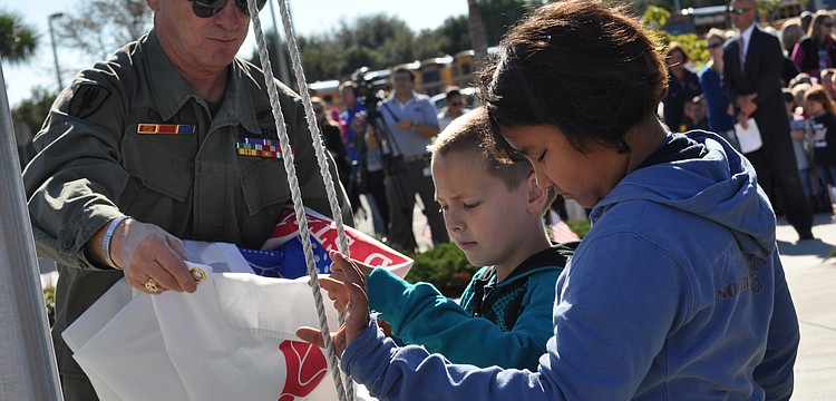 U.S. Army veteran  Billy Coffey assists students at Freedom Elementary School as they raise the Army's flag during a Veteran's Day ceremony today.