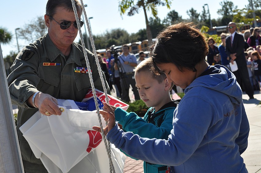 U.S. Army veteran  Billy Coffey assists students at Freedom Elementary School as they raise the Army's flag during a Veteran's Day ceremony today.