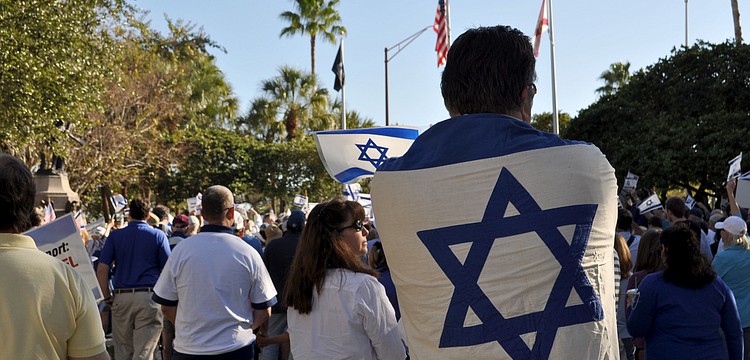 A man drapes the flag of Israel over his back in a show of support.
