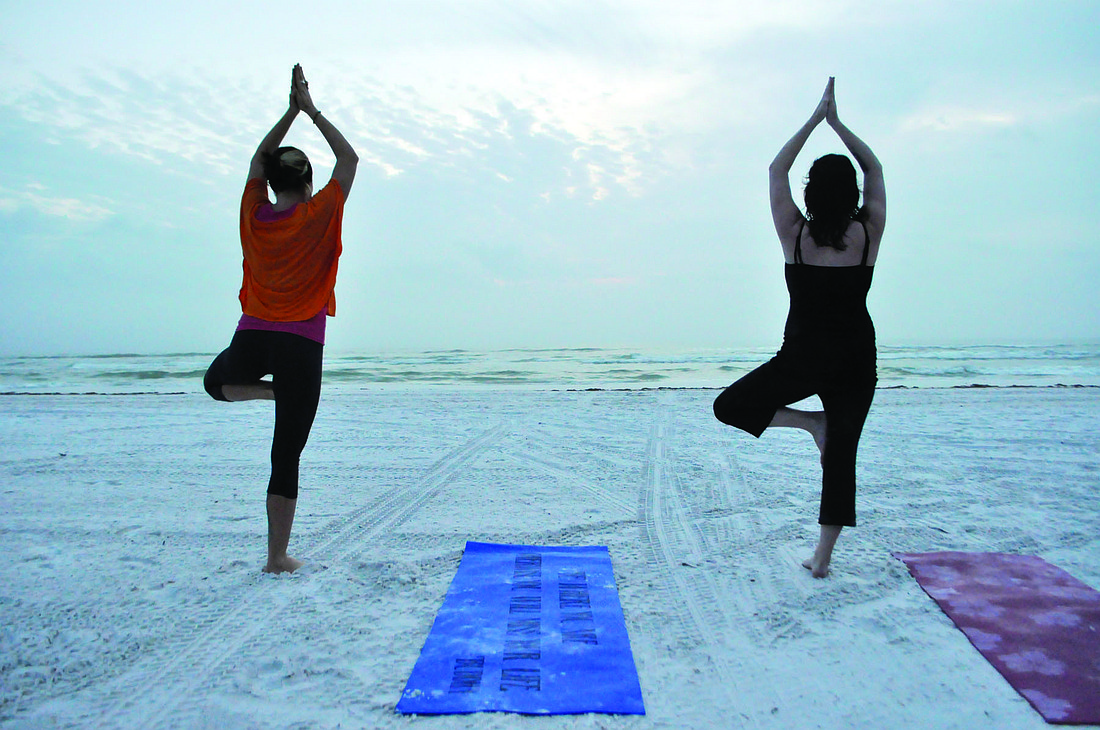 Courtney Kees leads Tabatha Giddens through a yoga class. Kees holds her sunset classes by the yellow lifeguard stand.