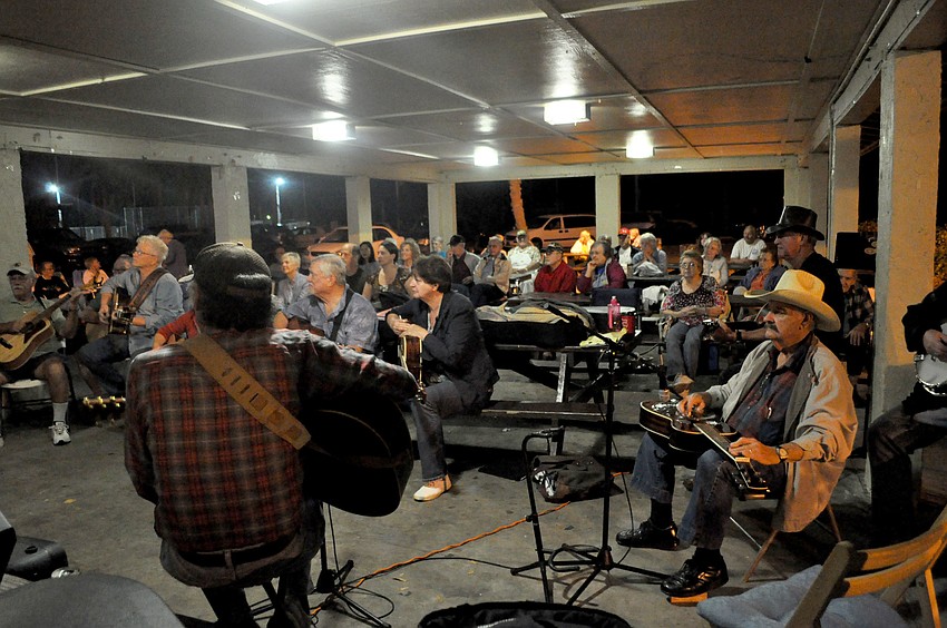 Bluegrass musicians perform in a circle at Bee Ridge Park as onlookers enjoy the music.