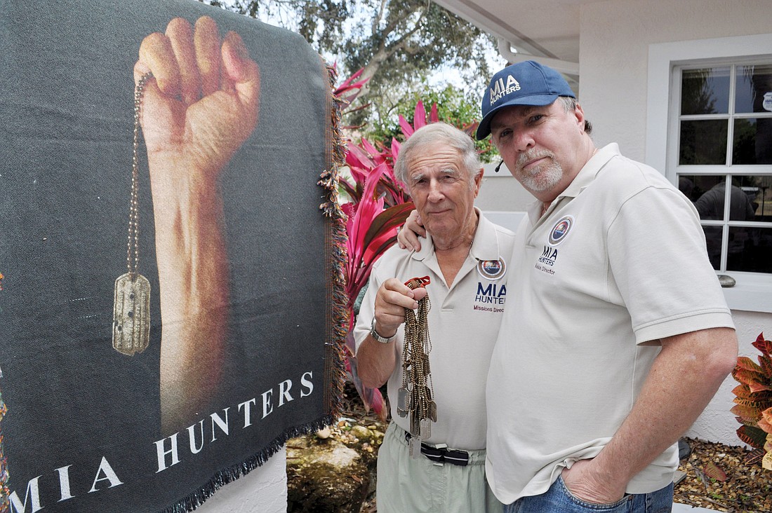 Bryan Moon stands with his son, Christopher, holding a collection of 22 dog tags recovered from the remains of MIA airmen in Papua, New Guinea.