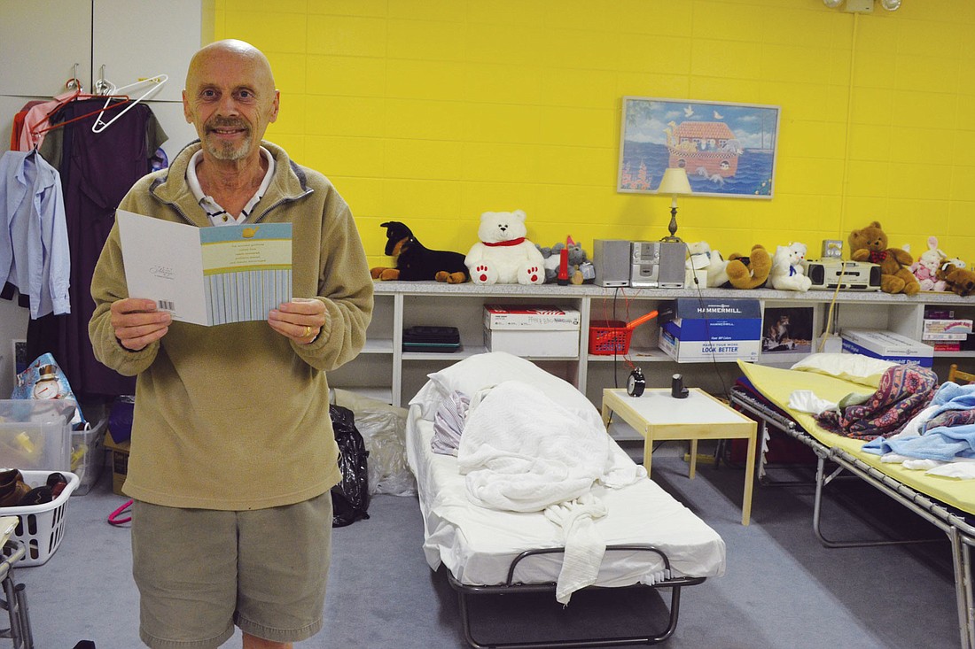 Family Promise Coordinator for St. Boniface David Mouatt holds a thank-you card in the classroom-turned-bedroom where the families stay.