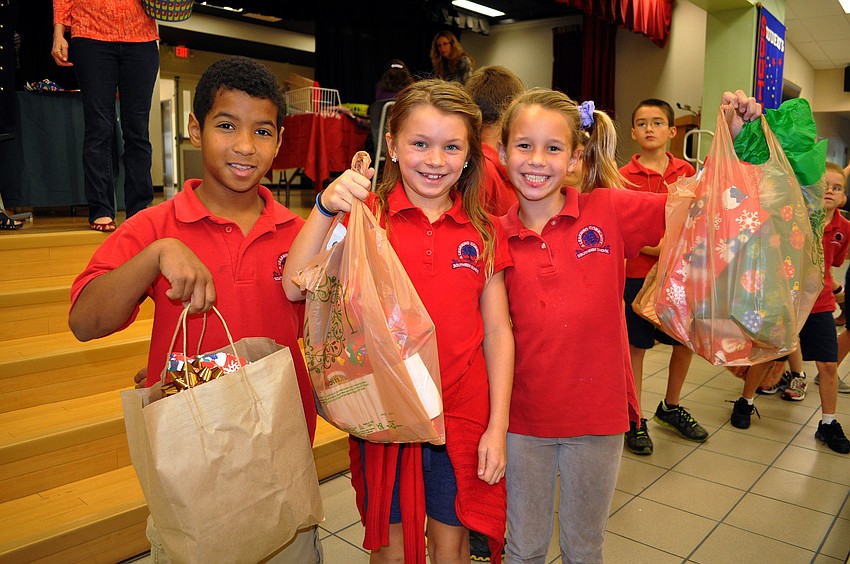 Fabiel Ortega, 9, Emily Hall, 8, and Emery Perez, 8, show-off their plastic bags full of wrapped gifts for their friends and family that they bought Tuesday, Dec. 4, at the Holiday House.