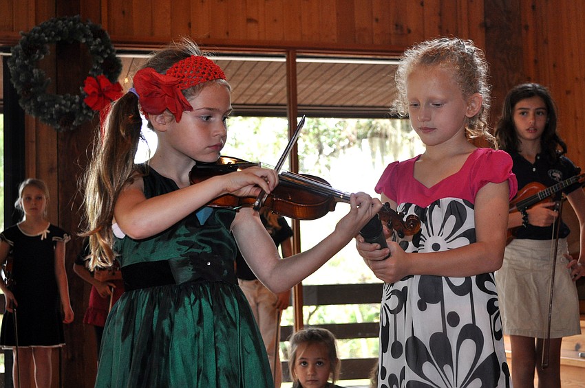 Claire Giraud holds the microphone up to Esabella Lerarioâ€™s violin as she plays a verse of â€œO Come Little Childrenâ€.