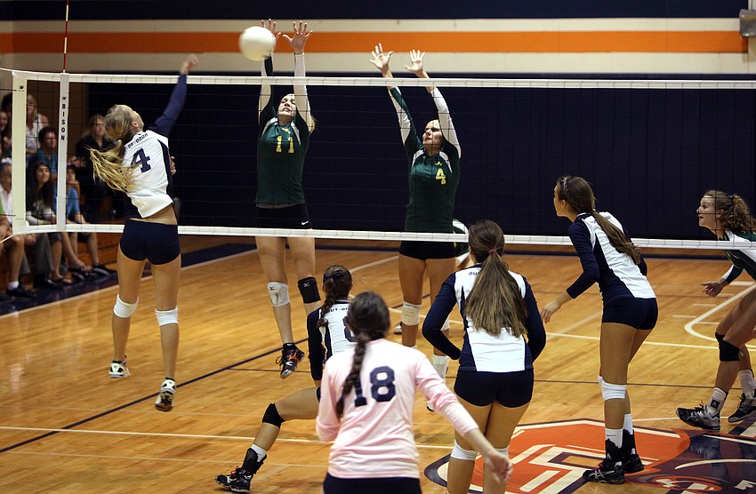 Natalie Buffett, No. 4, spikes the ball towards Amanda Everhardus, No. 11, and Gabrielle Woodruff, No. 4.