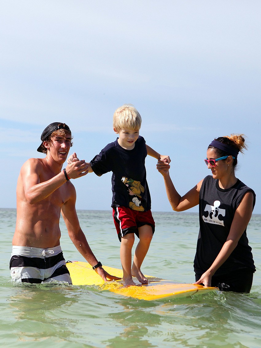 Keith Misja and Kate Maccarone help Drew Wojick, 5, ride on a surfboard Saturday, Sept. 15 during Hang 10 for Autism.