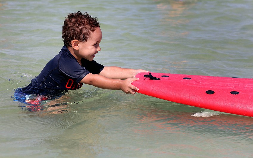Gavin Monteforte, 3, has fun pushing a surfboard in shallow water.