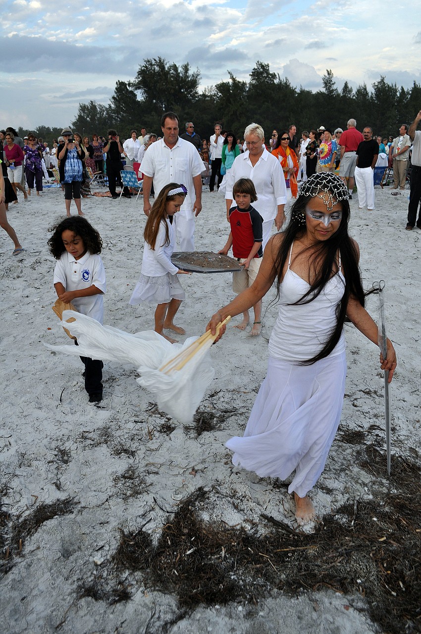 Dr. Margerite Barnett leads the way down to the water followed by Aukon Rivero who thre dried rose petals, followed by Ella and Gabriel Mirman carrying the mandala sand and Rev. Jim Toole and Rev. Eileen kemp behind them.