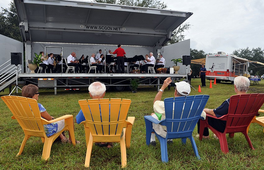 People sit in colorful, plastic, Adirondack chairs while watching the Sarasota Concert Band perform Wednesday, Oct. 3, the opening day of the Phillippi Farmhouse Market.