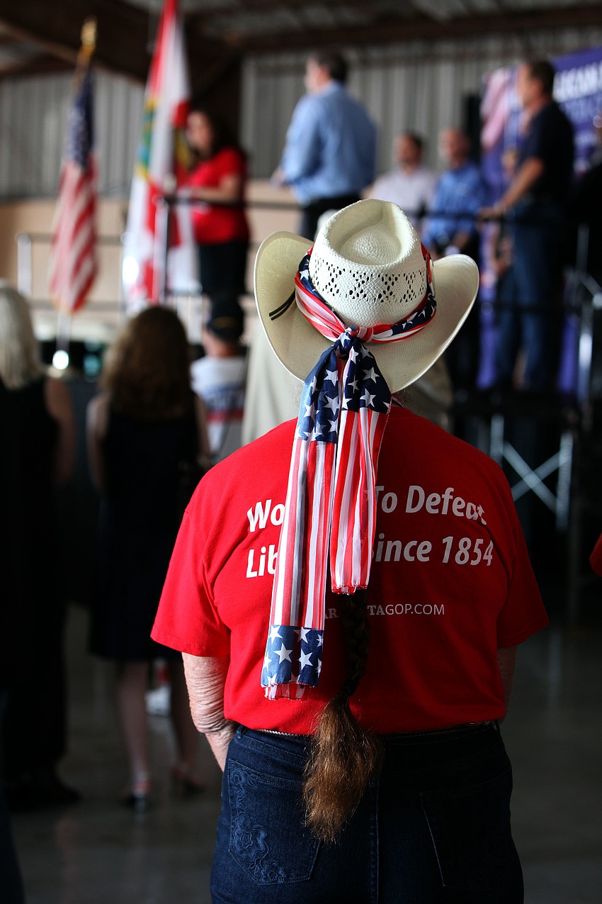 A woman wearing a cowboy hat with an American flag scarf wrapped around it watches the different politicians talk on stage Saturday, Nov. 3, at Dolphin Aviation.