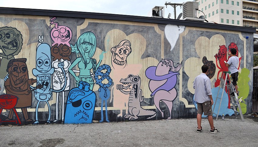 Stephen Palladino, of Clearwater, works on a mural on the side of the Shamrock Pub as Wes Roos, of Tampa, looks on.