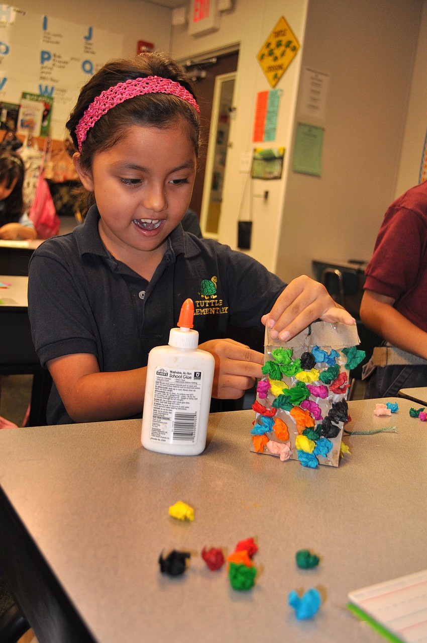 Brianna Cardenas works on gluing on pieces of colorful tissue paper onto a small, brown paper bag to create a piÃ±ata.