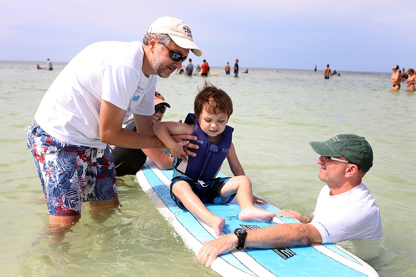 Andrew Burg along with Michelle Chrzczonowski and Bob Silverman help Nathan Burg, 3 Â½, get comfortable on a surfboard Saturday, Sept. 15 during Hang 10 for Autism at Siesta Key Public Beach.