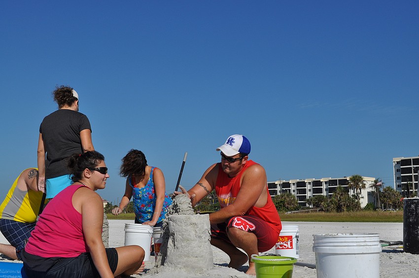 Newlyweds Elizabeth and Adam Rhodus demonstrate the â€œmix-scoop-plop-flatten-jiggleâ€ technique to create an arch for their sand castle.
