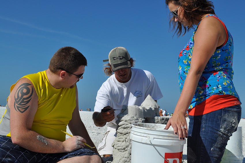 Local sand sculptor Andy Daily helps Travis and Lisa McCreary create their castle.
