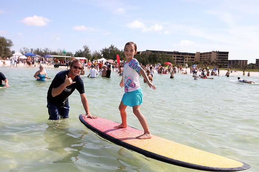 Dean Garati helps Abigail Pyott, 6, ride on a surfboard during Hang 10 for Autism Saturday, Sept. 15, at Siesta Key Public Beach.