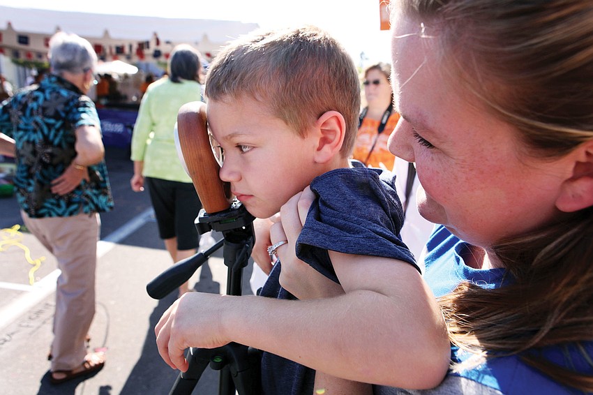 Valerie Glessing holds up her son, Austin, 5, to look through a viewfinder at 3-D chalk art.