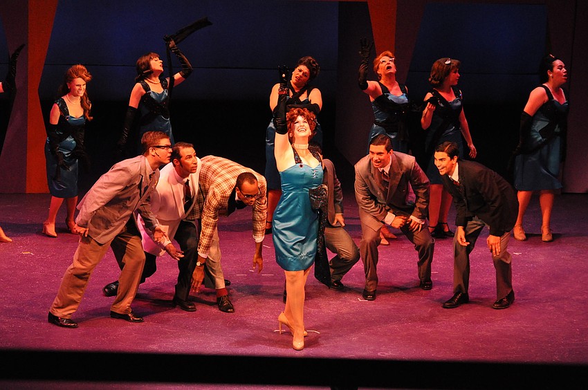 Danae DeShazer as Hedy LaRue with the businessmen and secretarial staff