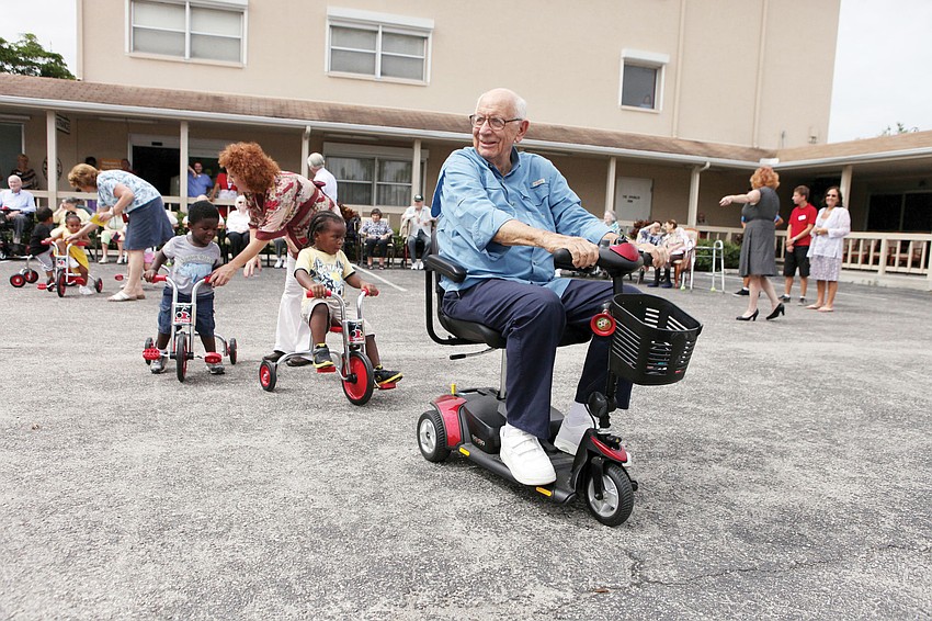 Bob Ireland leads the toddlers on his scooter in a game of â€œfollow the leader,â€ after the toddlers received brand new tricycles from the Rotary Club of Sarasota Bay.