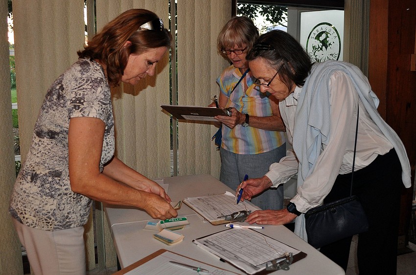 Dixie Stevens helps Freddie WindRiver and Nancy Aldrich sign in for the meeting and talk Thursday, Oct. 11, at the Sarasota Garden Club.