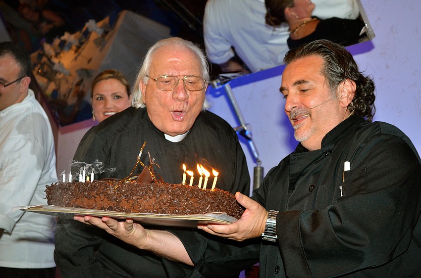 The Rev. Fausto Stampiglia blows out his birthday candles while Phil Mancini assists with holding the cake.