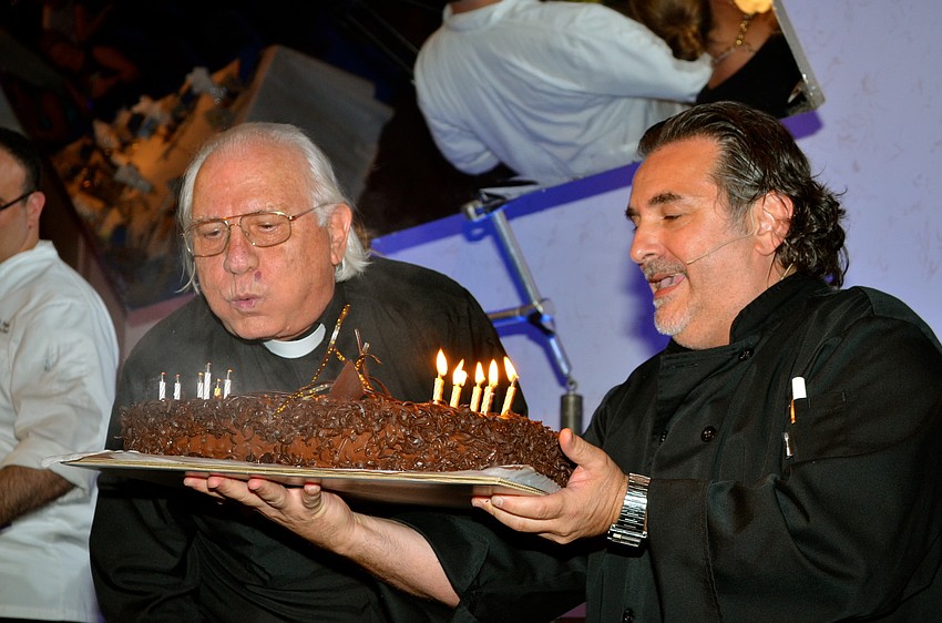 The Rev. Fausto Stampiglia blows out his birthday candles while Phil Mancini assists with holding the cake.