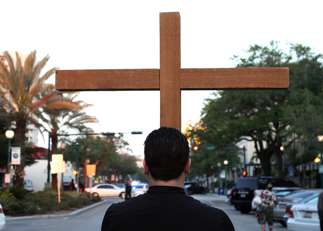 Chris Wood, the youth minister at Church of the Redeemer, carries the cross during the 13th annual Good Friday Morning Stations of the Cross walk.