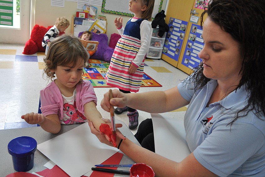 Alexis Simone, 3, gets her hands painted by teacher Jessica Gant, as part of hat-making festivities.