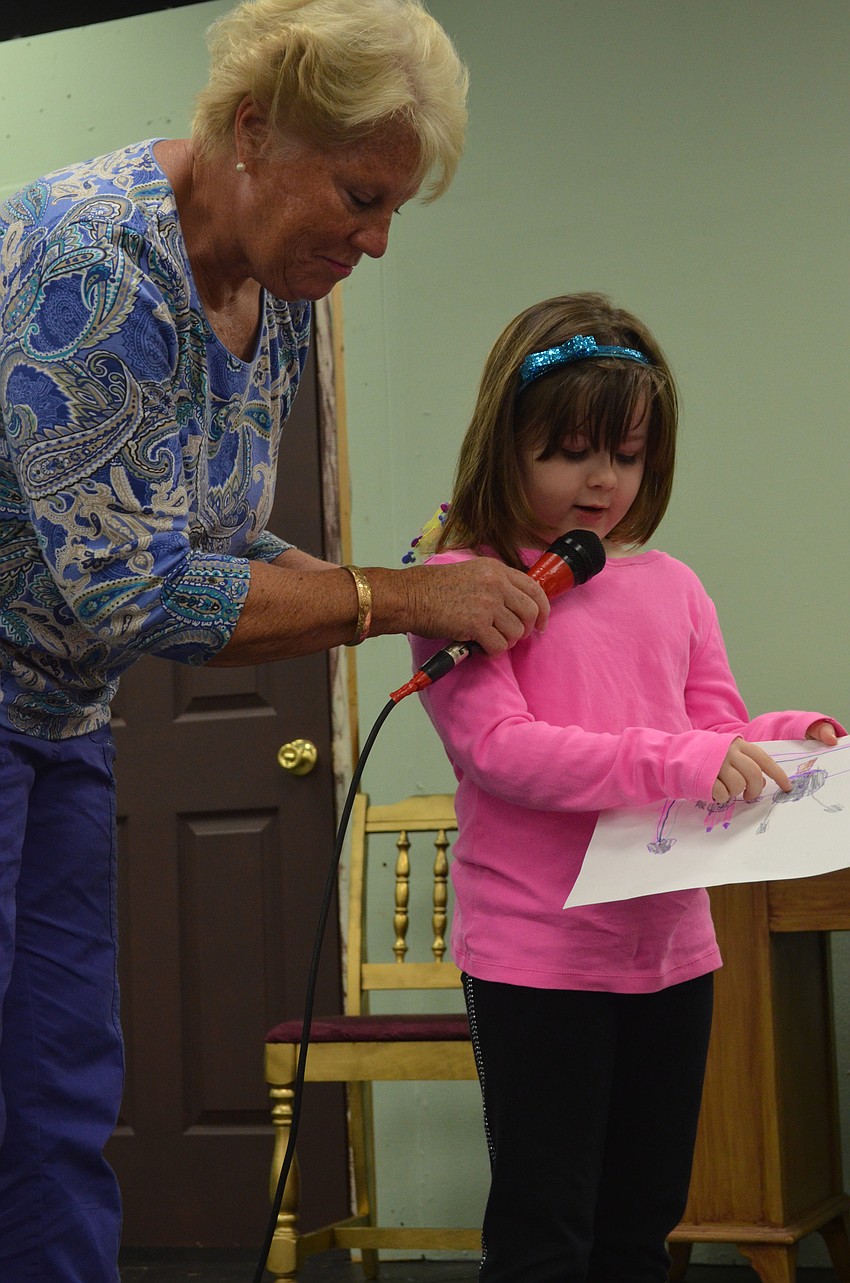 Preschool teacher Kathy Polen holds the microphone for preschooler Faith Romett as she explains her picture.