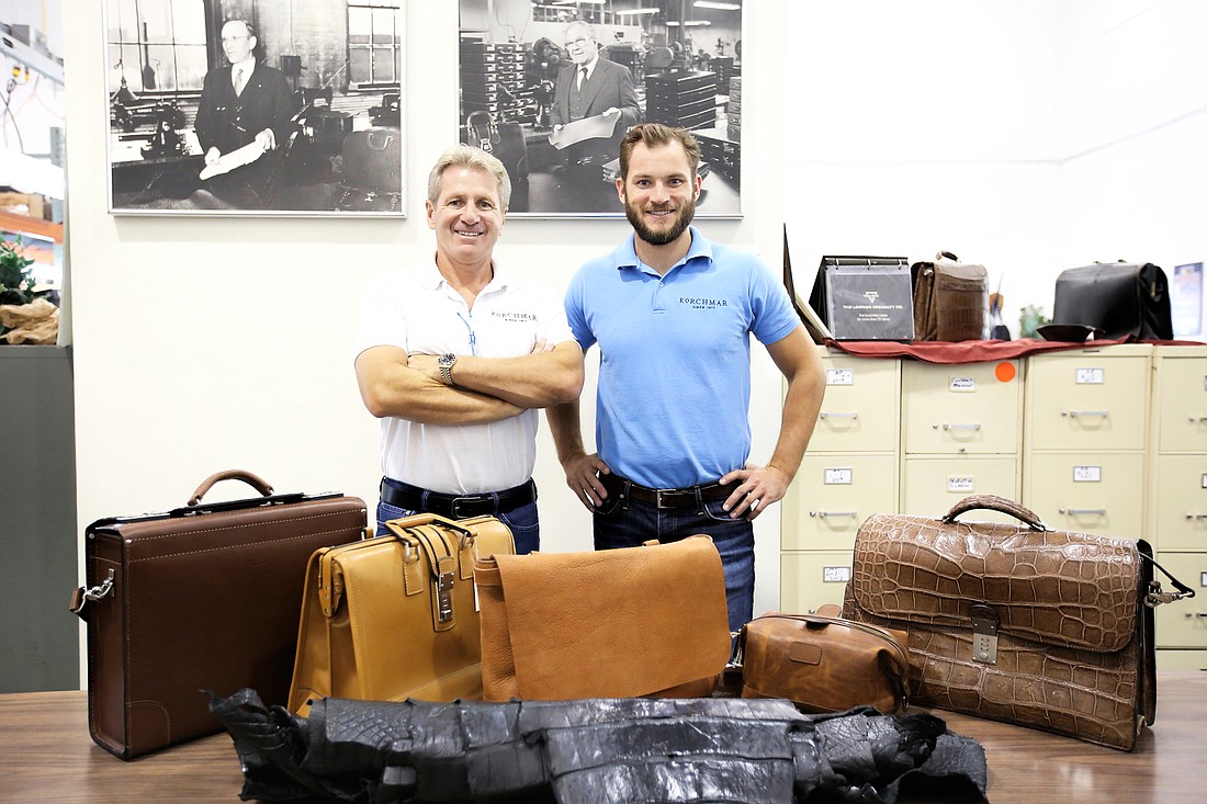 Michael (left) and Mike Korchmar display some of the luxury leather products the Naples-based company makes. Behind them are photos of Korchmar founder Max Korchmar (left) and second-generation owner Don. Photo by Stefania Pifferi