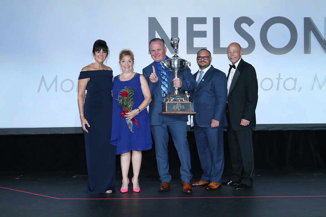 Joe and Sandy Nelson, holding a trophy and rose, joined on the far left by Mary Kennedy Thompson, Neighborly COO of franchise brands, and Mike Bidwell, Neighborly president and CEO, on the far right.