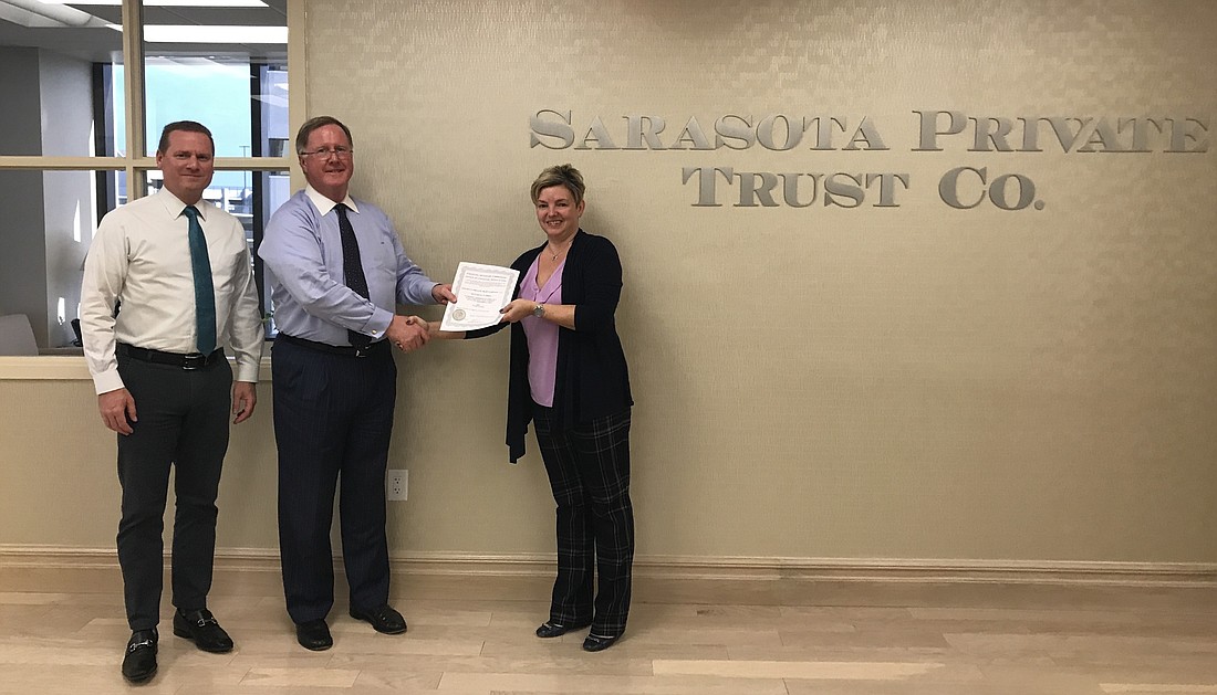 Courtesy. Sarasota Private Trust Co. CEO John Hart, center, with Senior Director Brian Volner, left, receiving the new charter from Florida Office of Financial Regulation official Angela Lerma.