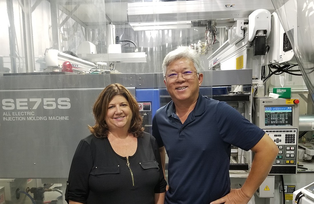 Courtesy. Michelle Perkins and Tung Nguyen in front of the dry molding machine used in the start of production of contact lenses. They oversee the Sarasota manufacturing and operations of Extreme H2O contact lenses.