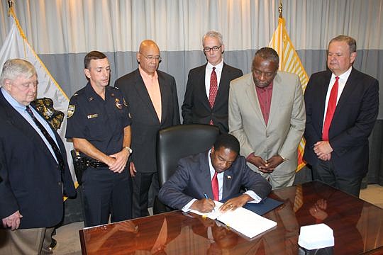Mayor Alvin Brown signs the pension reform bill into law as John Keane, left, and members of the Police and Fire Pension Board look on.