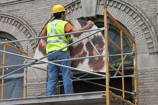 A worker with Elkins Constructors on Tuesday takes down one of the final jaguar panels from the Bostwick Building. Visible work on the Downtown structure is underway this week.