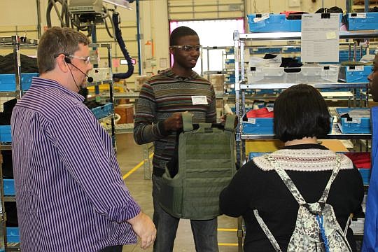 Robert E. Lee High School student Sean Edwards Jr. holds up a protective vest whose components were made at Safariland. At left is Bynne Harris, a production supervisor, who provided a tour Friday of the North Jacksonville manufacturer to the students.