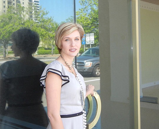 Julie Larsen stands at the door of the San Marco building at Prudential Drive and Kings Avenue that she plans to turn into one of two Julie's Urban Grocery stores. The glass reflects a nearby high-rise in the neighborhood.