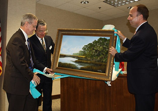 Photos by Joe Wilhelm Jr. - Former JEA Managing Director and CEO Jim Dickenson (left) unwraps a gift from JEA in recognition of his 40 years of service to the utility. Current CEO Paul McElroy and board of directors Chairman Ashton Hudson (right) hold...