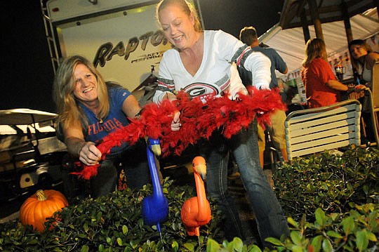 Best friends, Angela Beldsoe, left, of Jacksonville, a Gator fan, and Dorothy Callahan, right, of Callahan, a Bulldog fan, have a small disagreement as Callahan tries to put a Bulldog-themed boa over Bledsoe's Gator-themed flamingos as they decorate t...
