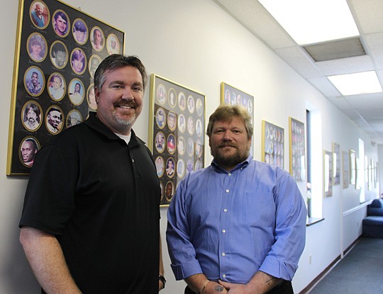 Photo by Marilyn Young - Ryan Backmann (left) and Carl Harms walk past dozens of frames of pictures of homicide victims that line the walls of their second-floor office at Compassionate Families.